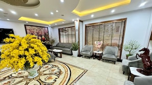 A modern lobby with a sofa, armchairs, a decorative rug, and a large floral arrangement. - Green Hadong Hotel (Hanoi)