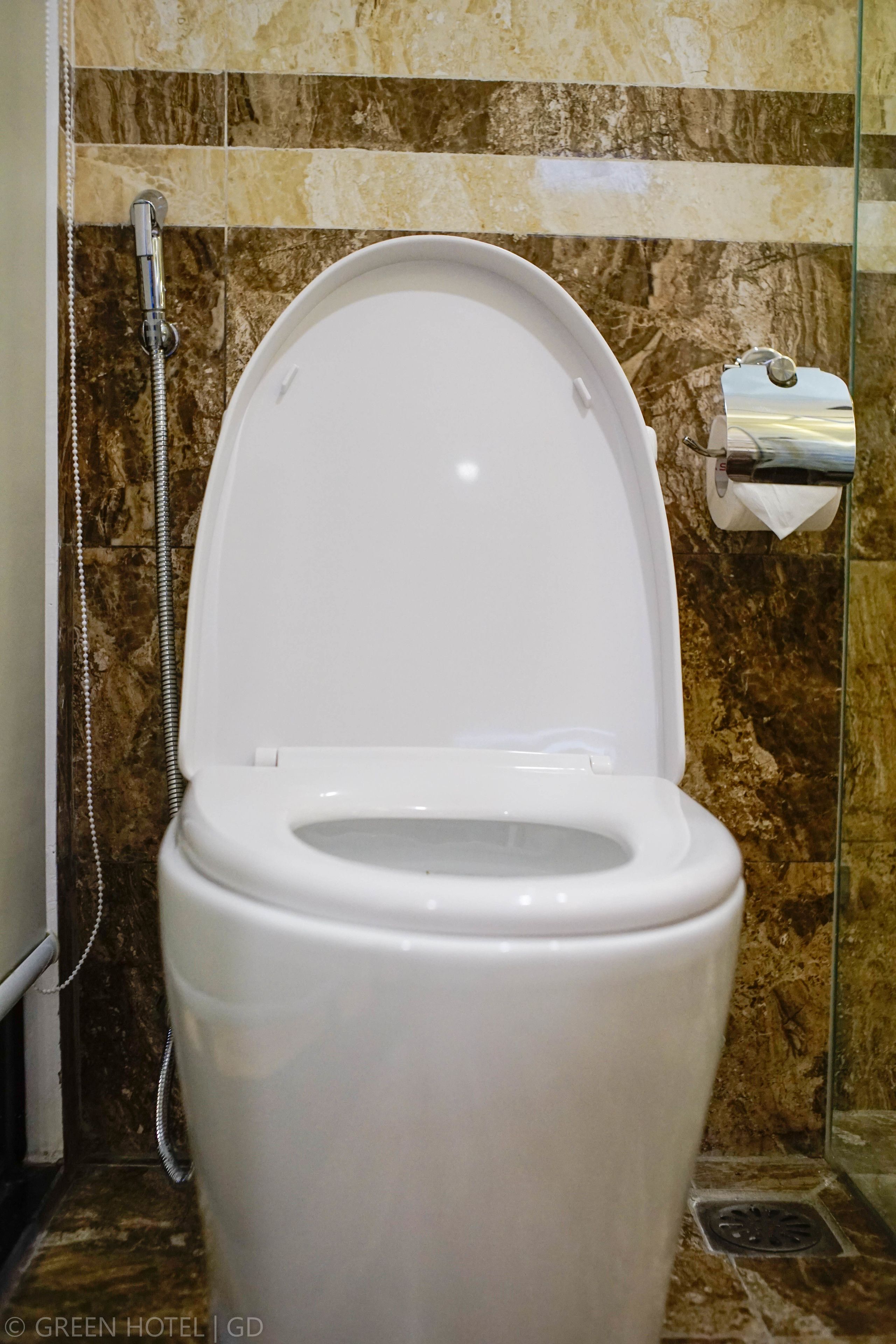 Des toilettes blanches avec un abattant fermé, dans une salle de bain aux murs de marbre et dotée d’une cabine de douche en verre.