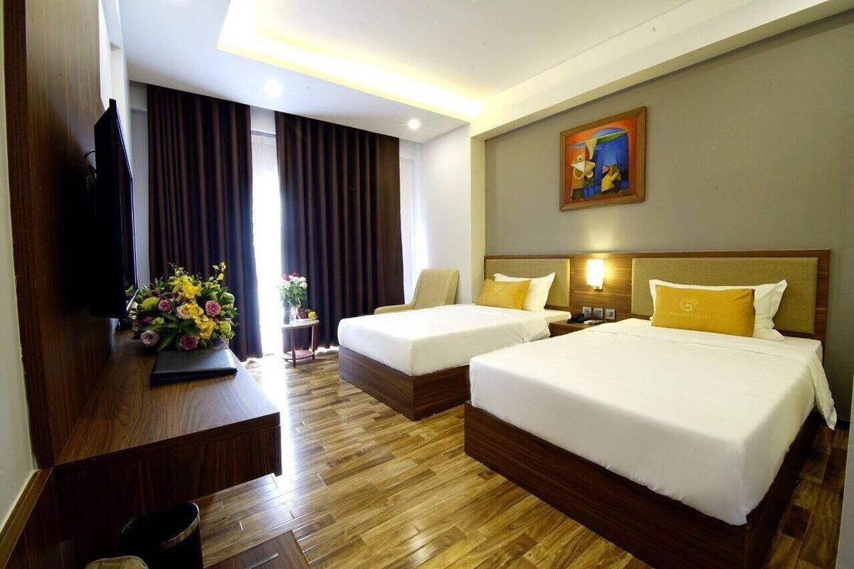 A hotel room with two beds, a desk with a laptop, a TV, and a painting on the wall.