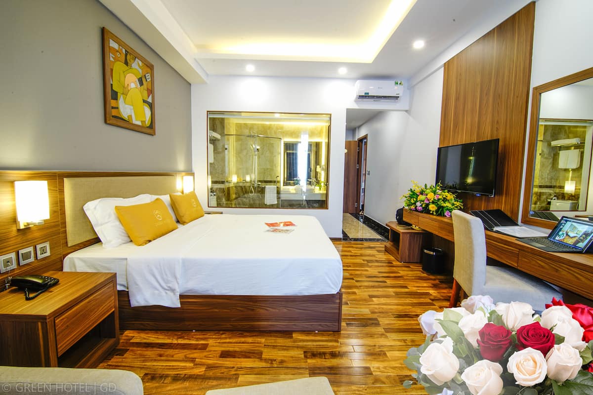 A hotel room with a bed, bedside tables, a desk with a laptop, a TV, and a large mirror.