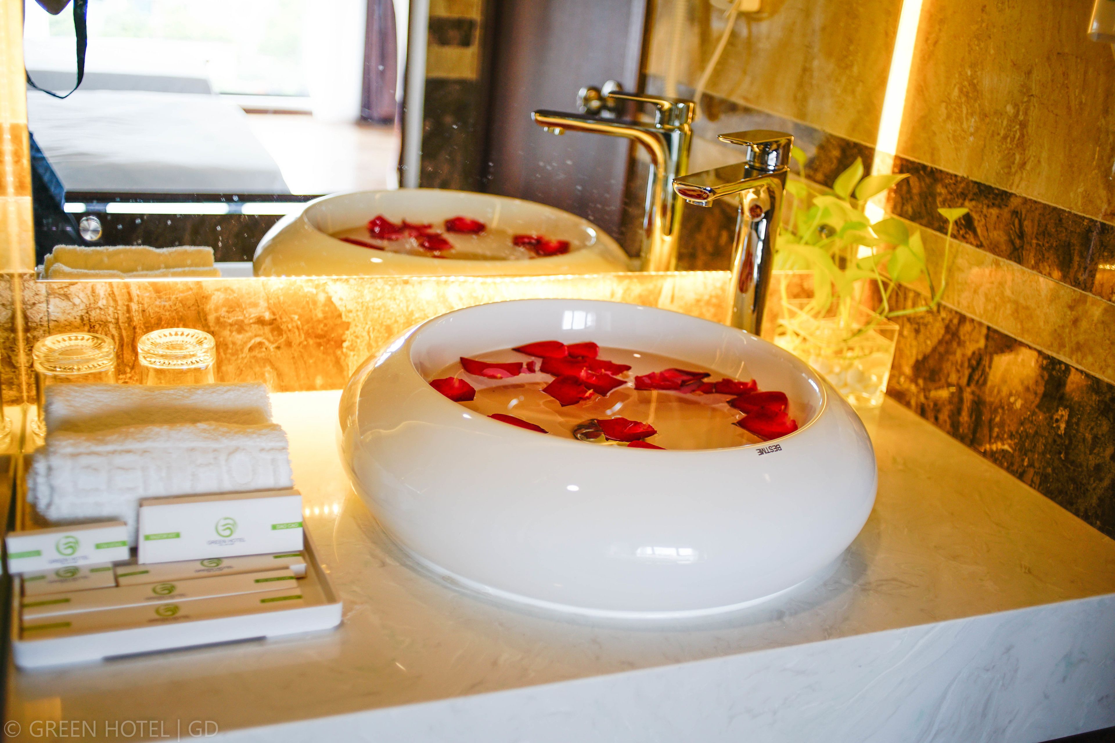 A bathroom with a white sink, rose petals in the water, a towel, and toiletries on the counter.