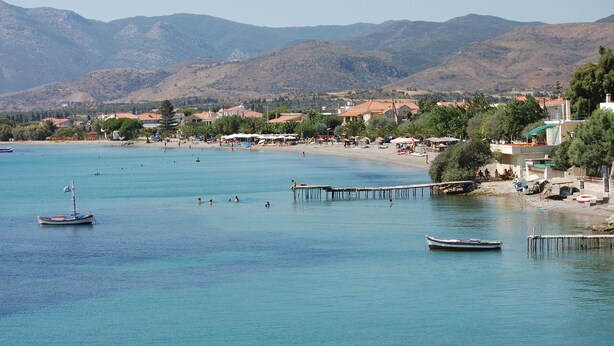 Un pueblo costero con playa, barcos y montañas al fondo.