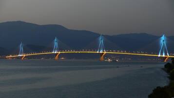 Een brug met meerdere torens en kabels, over een waterlichaam met bergen op de achtergrond.