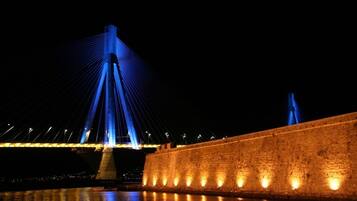 A nighttime view of a bridge with illuminated cables and a stone wall beside a body of water.