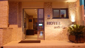Entrada de hotel con puerta de vidrio, un cartel sobre la puerta y una planta en maceta a la derecha.