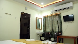 Ein Hotelzimmer mit Bett, Schreibtisch, Stuhl, Waschbecken, Spiegel und Fernseher.