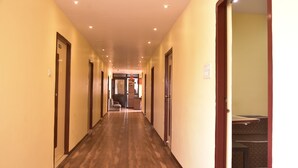 A hotel hallway with wooden flooring, doors on both sides, and a staircase at the end. - Hotel Drishti Inn (Nagpur)