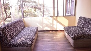 A room with two patterned sofas facing a large window with a view of trees. - Hotel Drishti Inn (Nagpur)