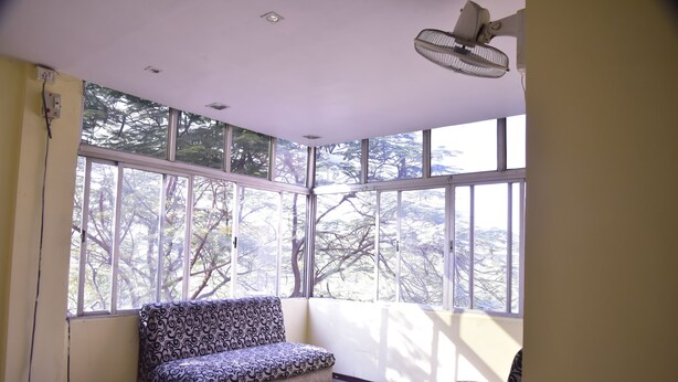 A room with a patterned sofa, large windows, and a ceiling fan. - Hotel Drishti Inn (Nagpur)