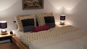 A bedroom with a bed, two bedside tables, a lamp on each table, a painting on the wall, and a wooden floor. - BellaCaro (Loehne)