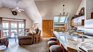 A spacious kitchen with a large island, wooden cabinets, and a chandelier. There is a dining area with a sofa and a table, and a ceiling fan. - Jackpine 8021 (Keystone)