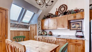 A kitchen with wooden cabinets, a dining table, and chairs. There are skylights and a chandelier. - Jackpine 8021 (Keystone)