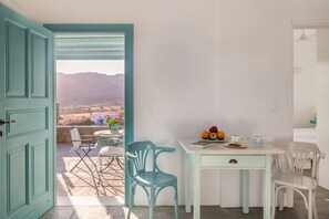 A room with a view of mountains, a table with fruits and a cup, and a chair.