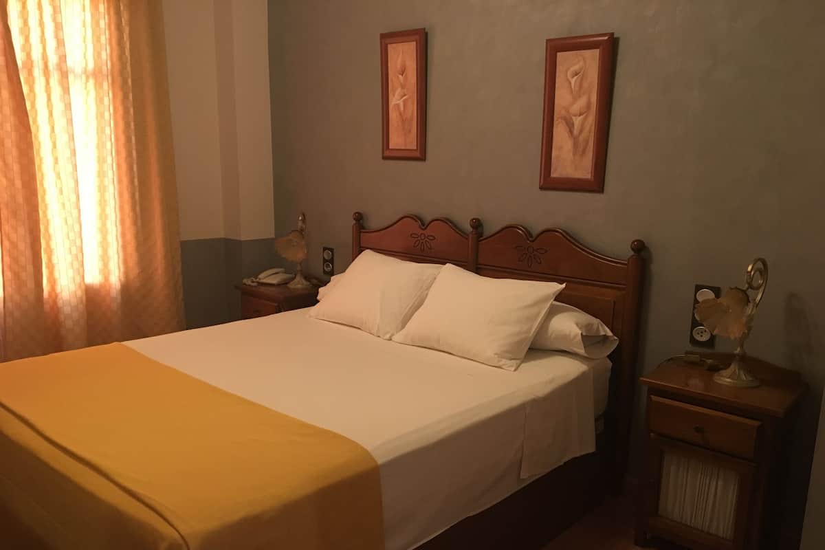 A neatly made bed with white linens, a wooden headboard, and two wall-mounted picture frames.