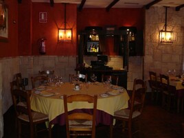 Un restaurante con pared de ladrillo, sillas y mesas de madera dispuestas con copas de vino y platos.