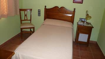 Un dormitorio con una cama de madera, una silla, una mesita de noche con lámpara y dos cuadros en la pared.