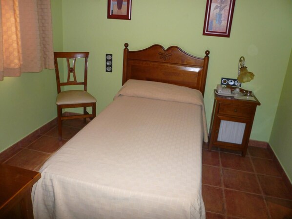 Un dormitorio con una cama de madera, una silla, una mesita de noche con lámpara y dos cuadros en la pared.