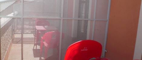 A red table with a chair, a white mesh screen, and a building in the background.