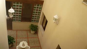 A courtyard with a fountain, potted plants, and two wall-mounted lanterns.
