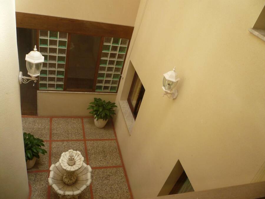 A courtyard with a fountain, potted plants, and two wall-mounted lanterns.