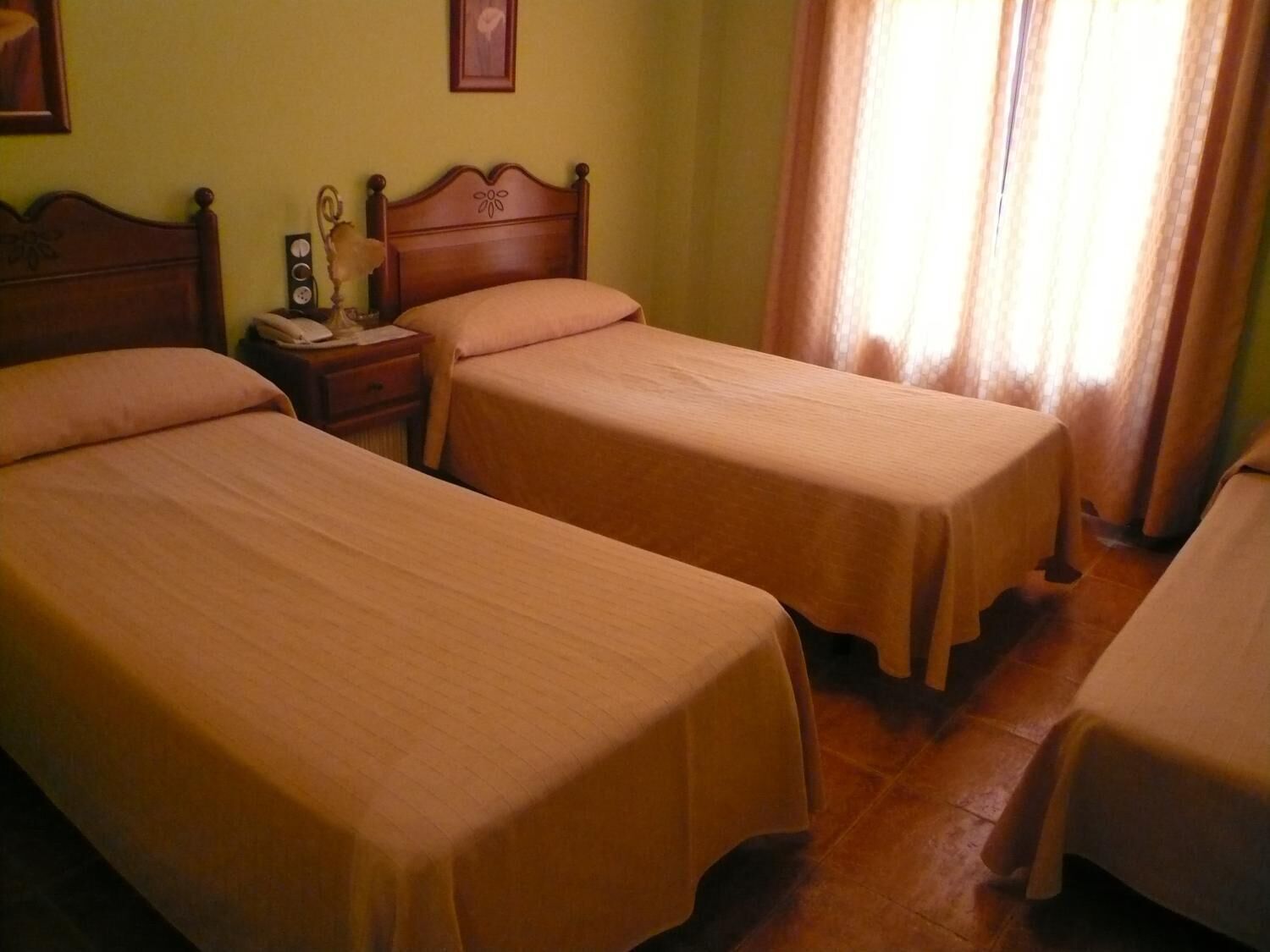 A room with two single beds, a nightstand with a lamp, and a window with curtains.