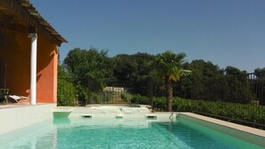 Una piscina cristalina con borde blanco, rodeada por una valla y vegetación.