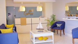 A modern living room with a sofa, armchair, and coffee table. There is a sign on the wall and a potted plant. - Hotel Capriccio Mare y Restaurante (Punta Cana)
