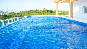 A swimming pool with a tiled edge, surrounded by a white building and greenery. - Hotel Capriccio Mare y Restaurante (Punta Cana)