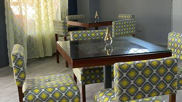 Un comedor con una mesa de vidrio, sillas estampadas, un ventanal hexagonal y una lámpara de techo.