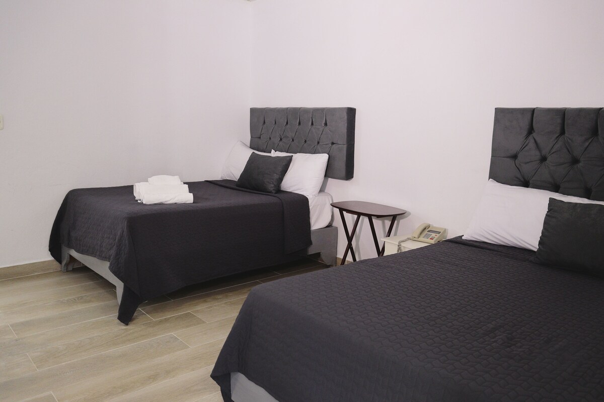 A hotel room with two beds, each with a dark headboard, a small bedside table with a telephone, and a light-colored floor.
