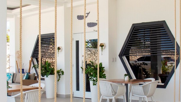 A modern dining area with white chairs, a wooden table, and a hanging swing. - Hotel Capriccio Mare y Restaurante (Punta Cana)