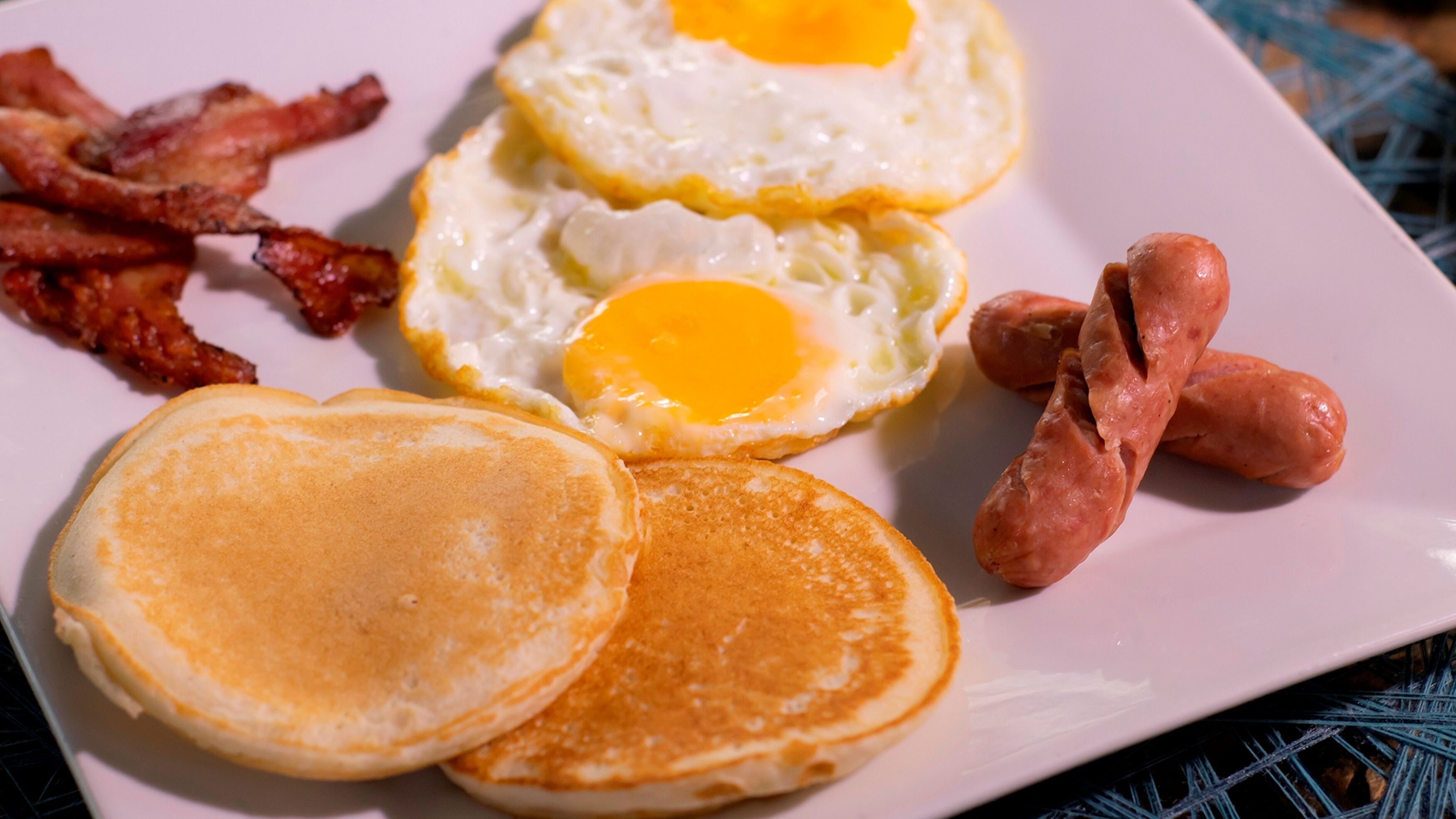 Un plato de desayuno con huevos, tocino, salchichas y panqueques.