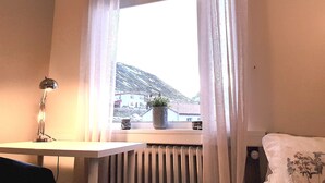 Ein Zimmer mit Fenster, Heizkörper, Schreibtisch, Lampe und einer Zimmerpflanze.