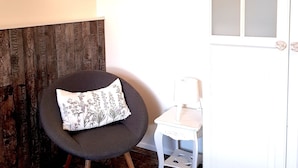 Ein Zimmer mit einem runden Sessel, einem kleinen Tisch, einer Wandleuchte und einer Tür mit satinierten Glasscheiben.