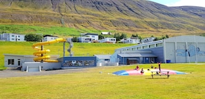 Un parque infantil con un tobogán amarillo y una estructura para escalar, frente a un fondo de casas y una montaña.