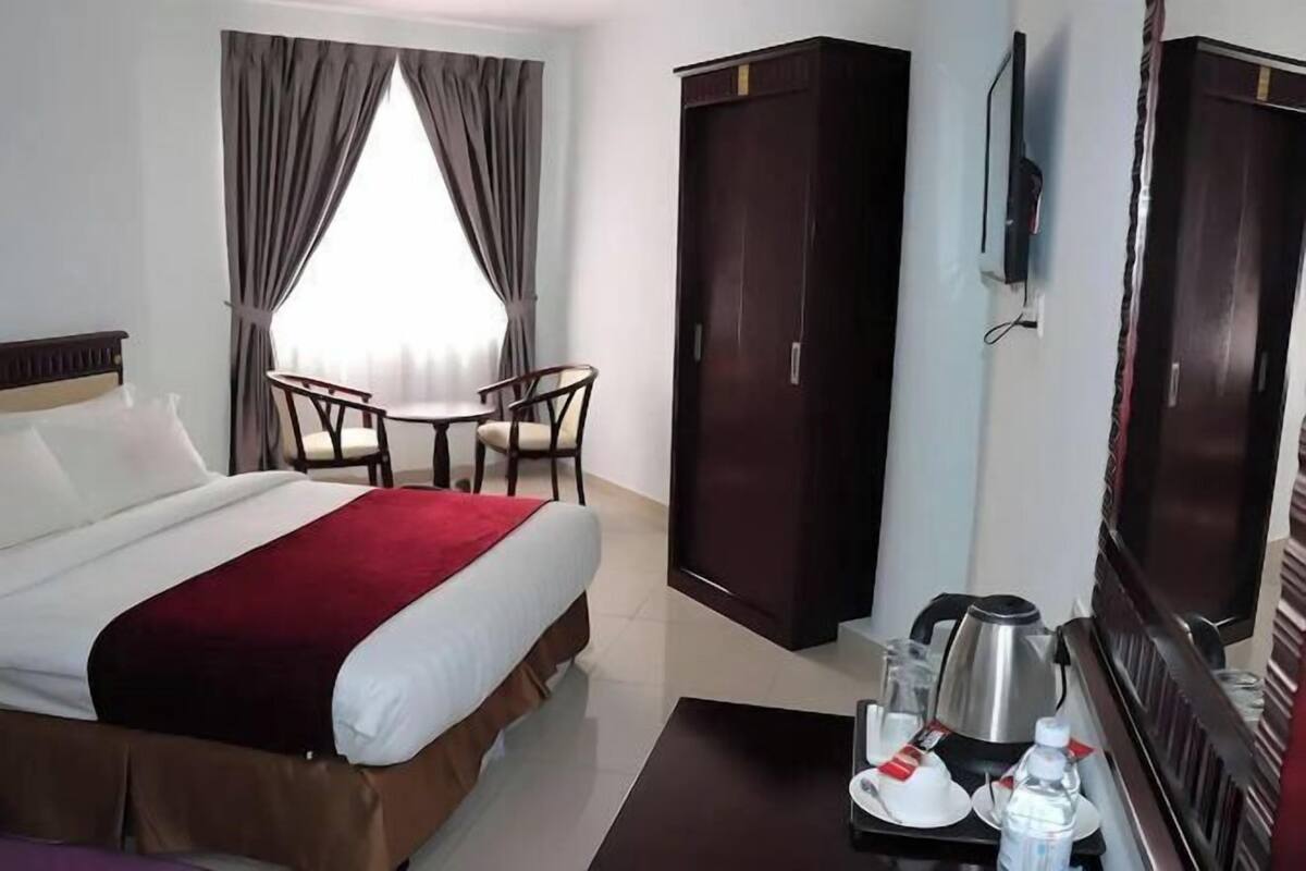 A hotel room with a bed, a desk with a chair, a wardrobe, a television, and a coffee maker.