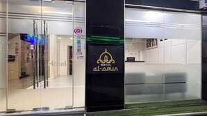 Ingresso moderno di un hotel con porte in vetro, un display digitale e un cartello che indica servizi come piscina e palestra.