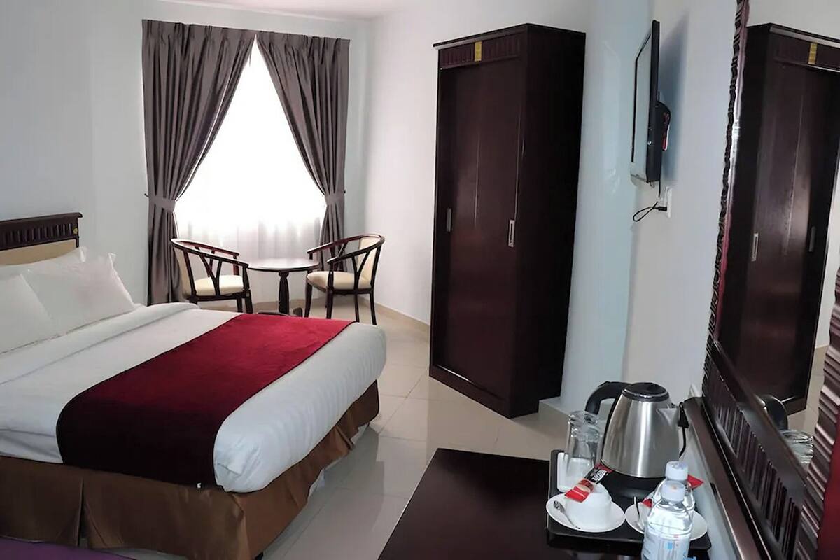 A hotel room with a bed, a desk with a chair, a wardrobe, a television, and a coffee maker.
