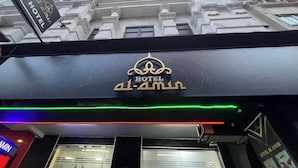 Segnaletica di un hotel con caratteri arabi e un logo, luci al neon e una facciata di edificio in stile classico sullo sfondo.