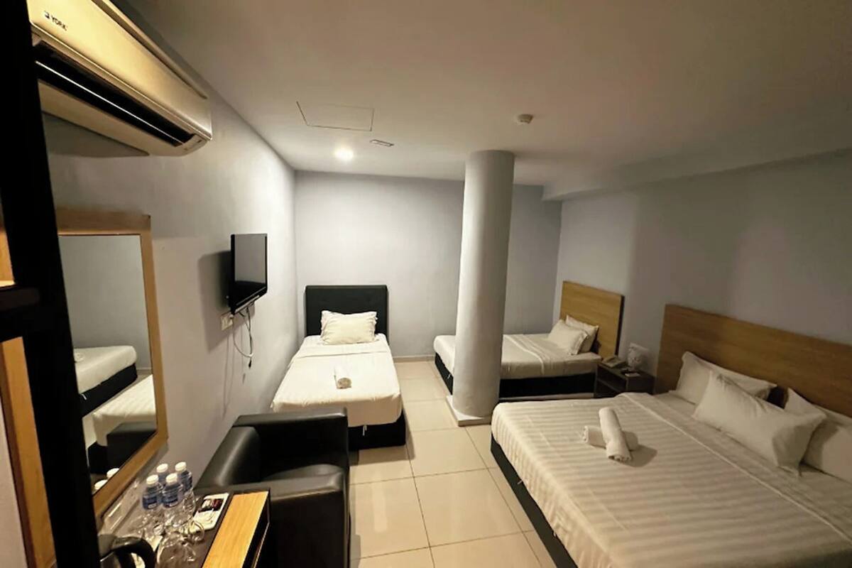 A hotel room with two single beds, a desk with a chair, a mirror, and an air conditioning unit.