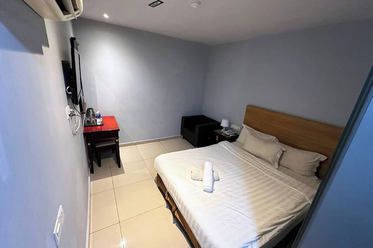 A hotel room with a bed, a desk, a chair, a TV, and a nightstand.