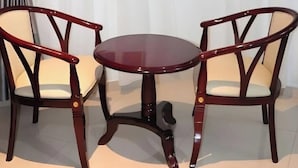 Una stanza con un tavolo rotondo in legno e due sedie abbinate, una finestra con tende leggere e una vista parziale di un letto.