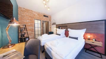 A hotel room with two beds, a desk with a lamp, a chair, a brick wall, and a wooden headboard.