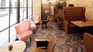 A cozy cafe with brick walls, large windows, and a mix of seating including plush armchairs and wooden tables.