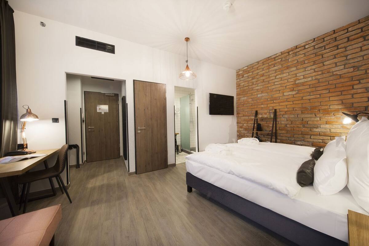 Habitación de hotel con cama, escritorio, silla y pared de ladrillo.