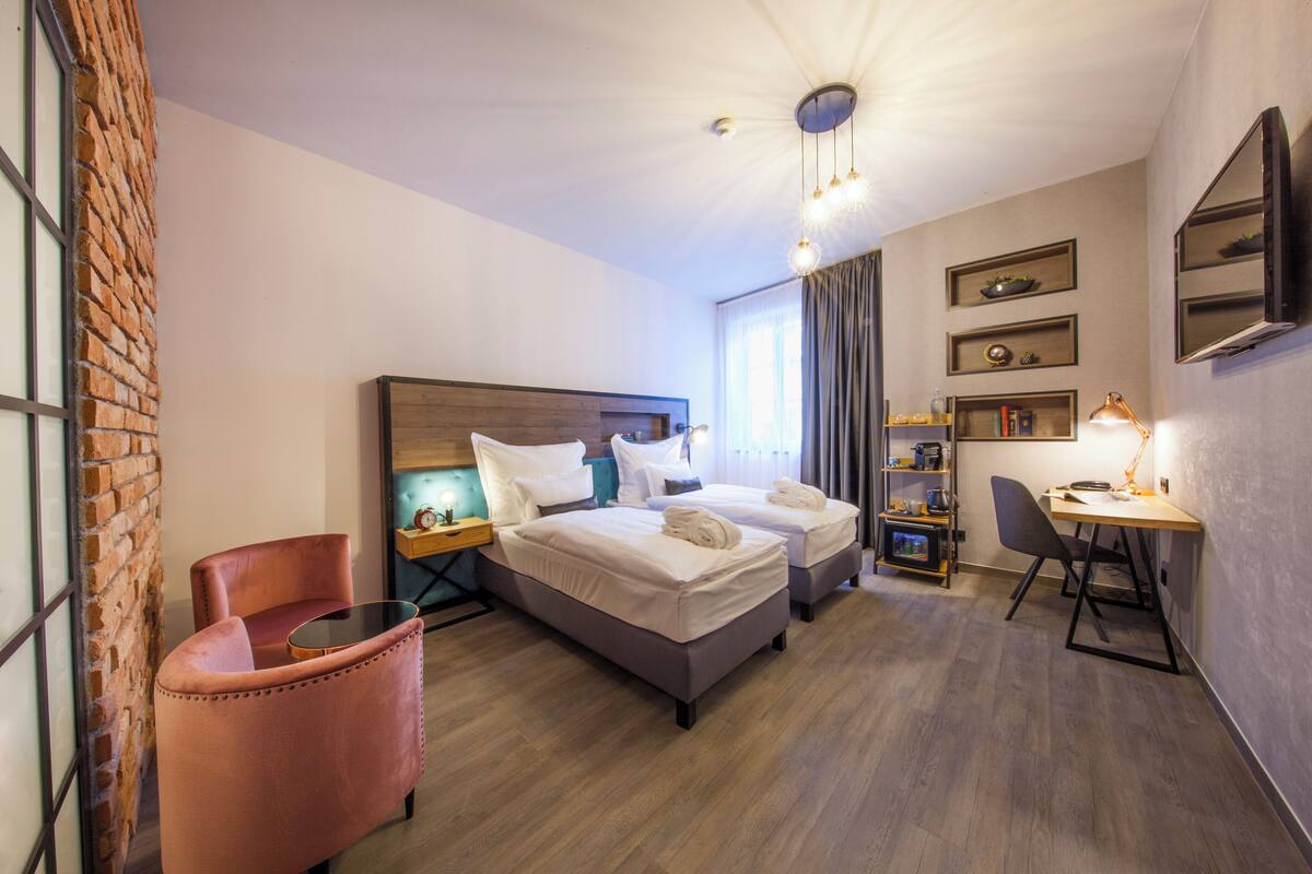 Una habitación de hotel con dos camas, un escritorio, una silla, una estantería y una pared de ladrillo.