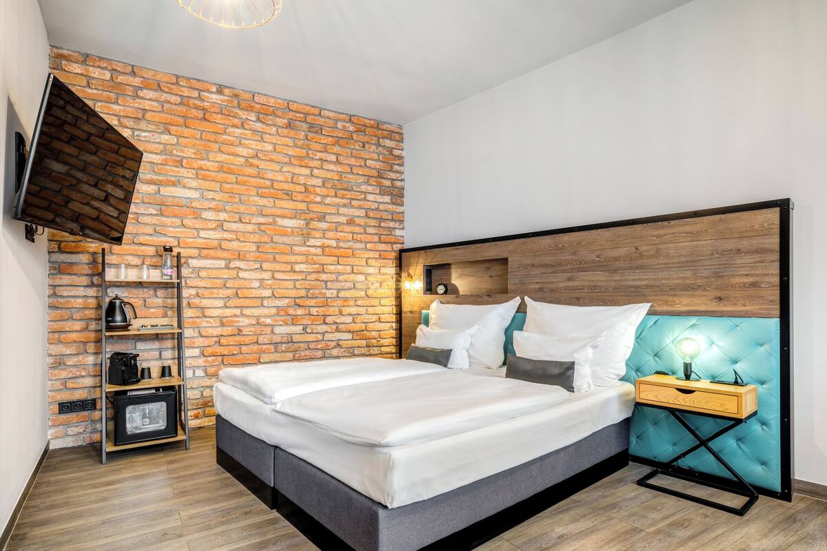 Un dormitorio moderno con pared de ladrillo, una cama grande, cabecero de madera, una mesita de noche y un televisor montado en la pared.