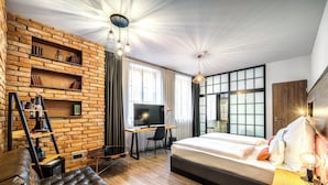 Una habitación de hotel moderna con pared de ladrillo, una cama grande, un escritorio con televisor y un sofá de cuero.