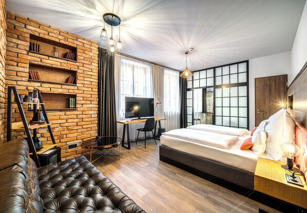 Quarto de hotel moderno com parede de tijolos, uma cama grande, uma escrivaninha com televisão e um sofá de couro.