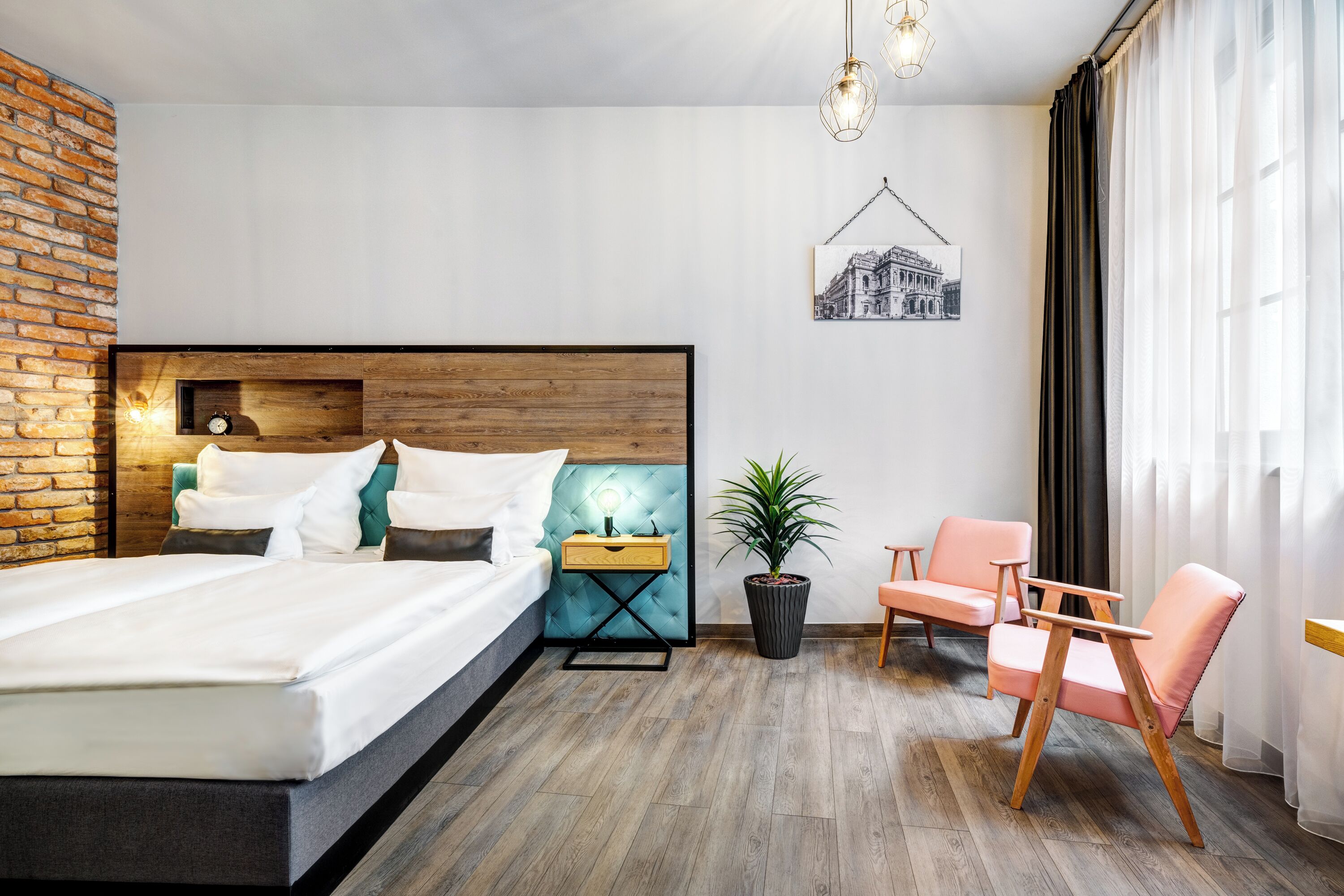 Et moderne hotelværelse med en stor seng, et natbord med lampe, en lille potteplante, en stol og et billede hængende på væggen.